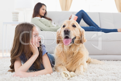 Girl looking at dog while lying on rug