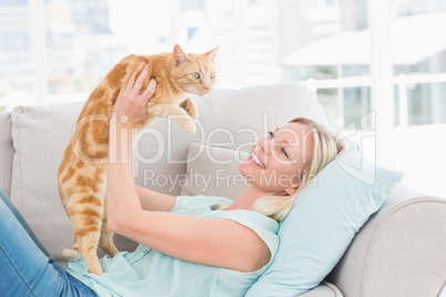 Woman lifting cat on sofa at home