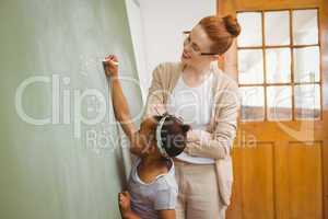 Teacher looking at girl write on blackboard in classroom