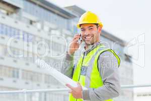 Smiling male architect with blueprints talking on mobile phone