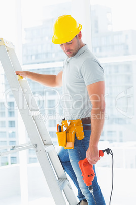 Manual worker with drill machine climbing ladder