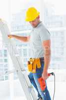 Manual worker with drill machine climbing ladder