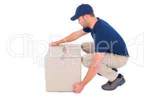 Delivery man crouching while picking cardboard box
