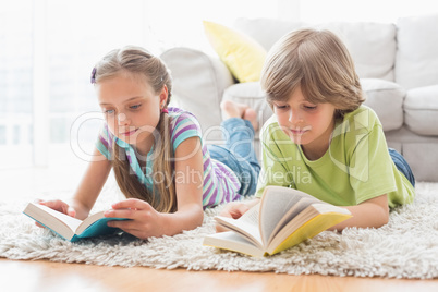 Siblings reading books while lying on rug