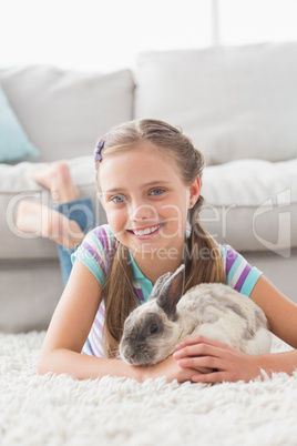 Smiling girl with rabbit lying on rug in living room