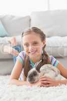 Smiling girl with rabbit lying on rug in living room