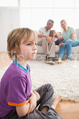 Sad boy sitting on floor while parents enjoying with sister