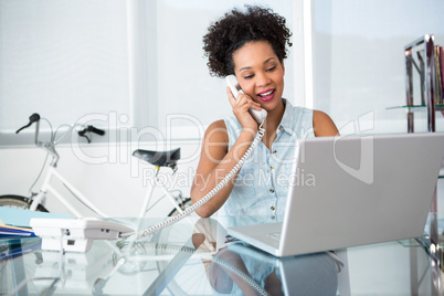 Young woman using telephone and laptop