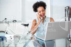 Young woman using telephone and laptop