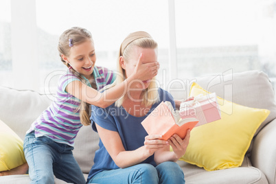 Happy girl surprising her mother with gift at home