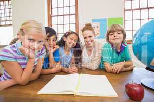 Cute pupils and teacher smiling at camera in classroom