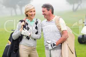 Golfing couple smiling and holding clubs