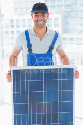 Smiling handyman holding solar panel in bright office