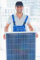 Smiling handyman holding solar panel in bright office