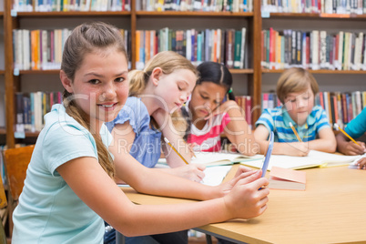 Cute pupil using tablet computer in library