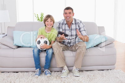 Happy boy watching soccer match with father on sofa