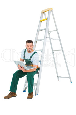 Carpenter sitting on ladder using laptop