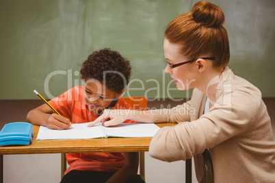 Teacher assisting little boy with homework in classroom