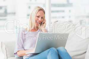 Woman talking on phone while using laptop on sofa