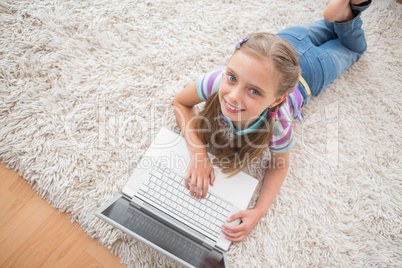 Cute girl using laptop while lying on rug