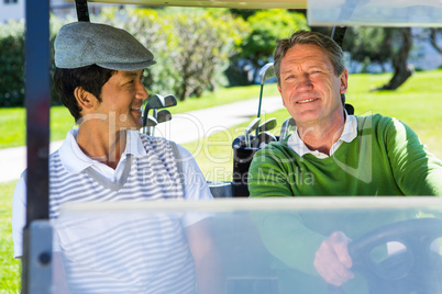 Golfing friends driving in their golf buggy smiling at camera