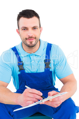 Plumber writing on clipboard while sitting on toolbox