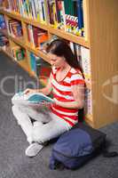 Pretty student sitting on floor reading book in library