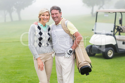 Happy golfing couple with golf buggy behind