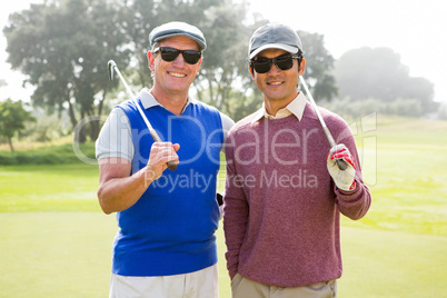 Golfing friends smiling at camera holding clubs