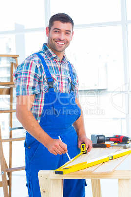 Smiling handyman using tape measure at workbench in office