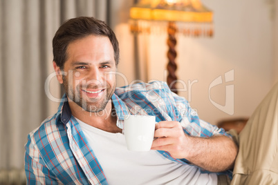 Handsome man relaxing on his bed with hot drink