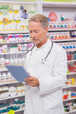 Concentrated senior pharmacist using tablet