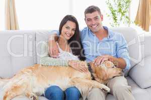 Happy couple stroking dog while sitting on sofa