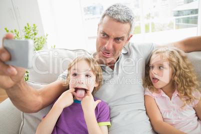 Father making face while taking selfie with children