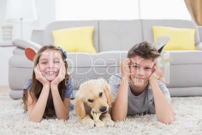 Happy siblings with puppy lying on rug