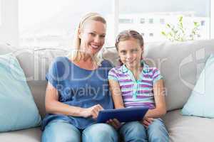 Happy mother and daughter using digital tablet on sofa