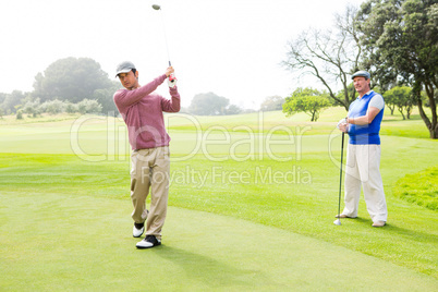 Golfer swinging his club with friend behind him