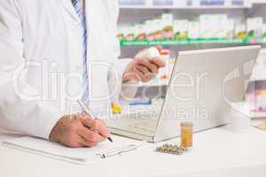 Pharmacist writing on clipboard and holding medication