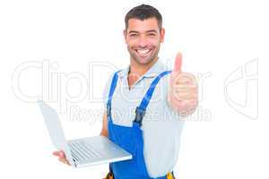 Portrait of handyman with laptop gesturing thumbs up