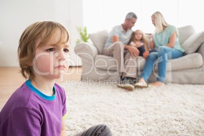 Upset boy sitting on floor while parents enjoying with sister