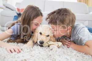 Siblings kissing puppy on rug