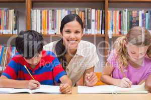 Pretty teacher helping pupils in library