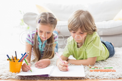 Siblings drawing with colored pencils while lying on rug