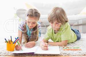 Siblings drawing with colored pencils while lying on rug