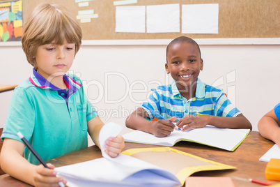 Cute pupils writing at desk in classroom