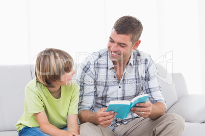 Happy father reading story for boy on sofa