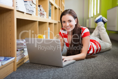 Student using laptop lying on library floor