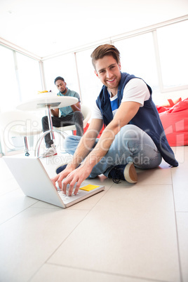 Smiling young man using laptop on floor