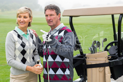 Happy golfing couple with golf buggy behind