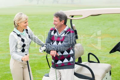 Happy golfing couple with golf buggy behind